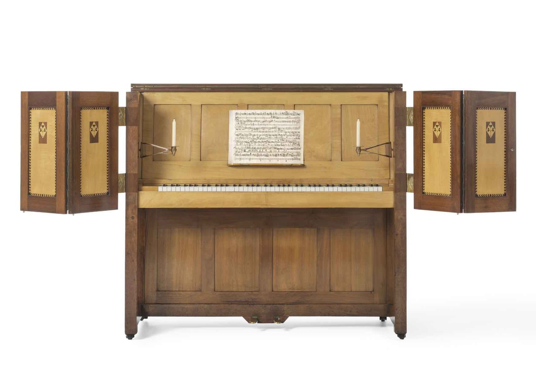 Antique upright cabinet piano with hinged inlaid doors open, brass candle sconces, and sheet music on the stand.