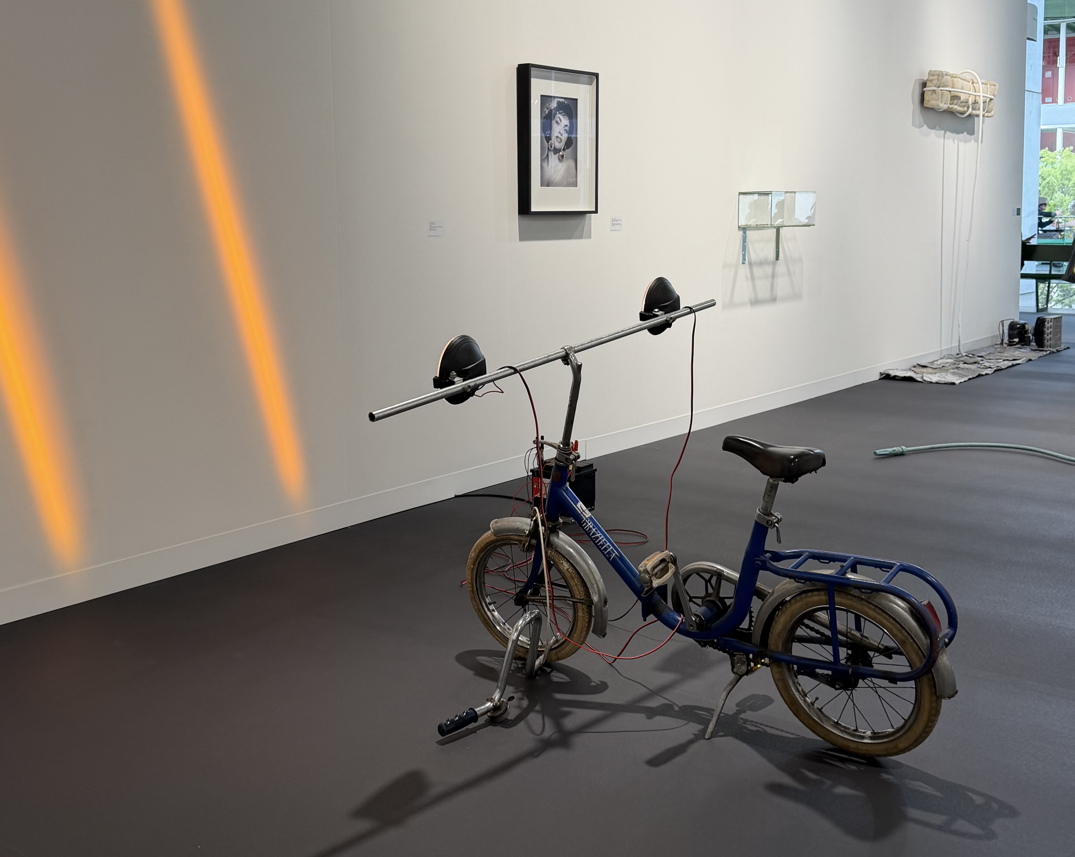 Modified blue folding bicycle sound sculpture with two black speakers on extended handlebar in a gallery space