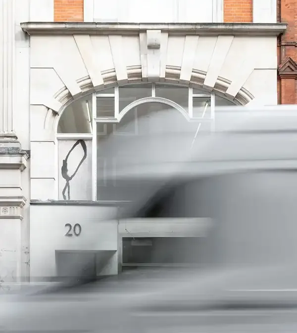 Des Bains entrance at number 20 with white arched window and stone facade, blurred vehicle passing in motion