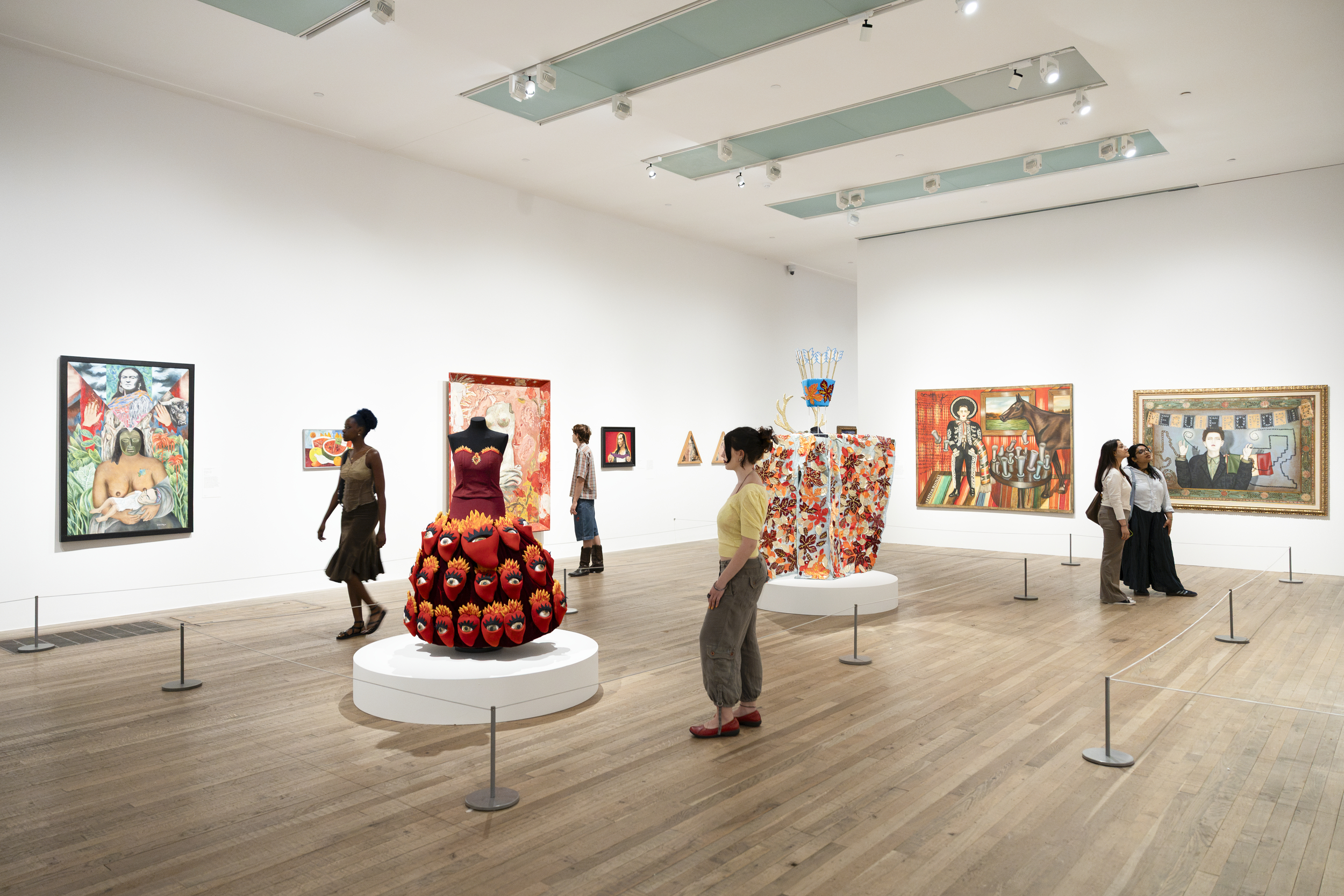 Visitors view colourful paintings and sculptural dresses at Frida: The Making of an Icon exhibition gallery